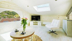 Un dormitorio tipo loft moderno con tragaluces, un televisor de pantalla plana, un sofá blanco y una mesa de comedor con un jarrón de flores.