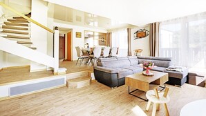 Una sala de estar moderna con una escalera, un sofá gris, una mesa de centro de madera y un área de comedor con sillas y una mesa.
