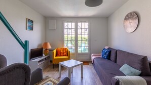 Uma sala de estar com sofá, poltrona, televisão e um relógio na parede.