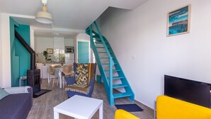Uma sala de estar com sofá, uma poltrona amarela, televisão e escada.