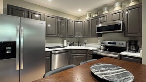 A modern kitchen with stainless steel appliances, a wooden dining table, and grey cabinetry.