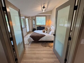 A bedroom with a bed, bedside tables, a nightstand, a window with blinds, and a ceiling light fixture. - Granite Chutes - Luxury 2BR Retreat Near Schweitzer & Sandpoint (Sandpoint)