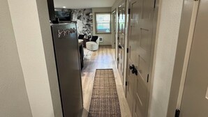 A hallway leading to a kitchen with a refrigerator, a rug, and a door with a handle.
