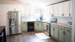 A modern kitchen with white cabinets, stainless steel appliances, and a wooden floor.