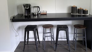 A kitchen with a black countertop, three stools, and shelves with kitchenware.