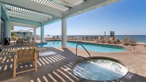 A covered pool area with lounge chairs and a hot tub, overlooking a beach. - The Colonnades 1901 (Gulf Shores)