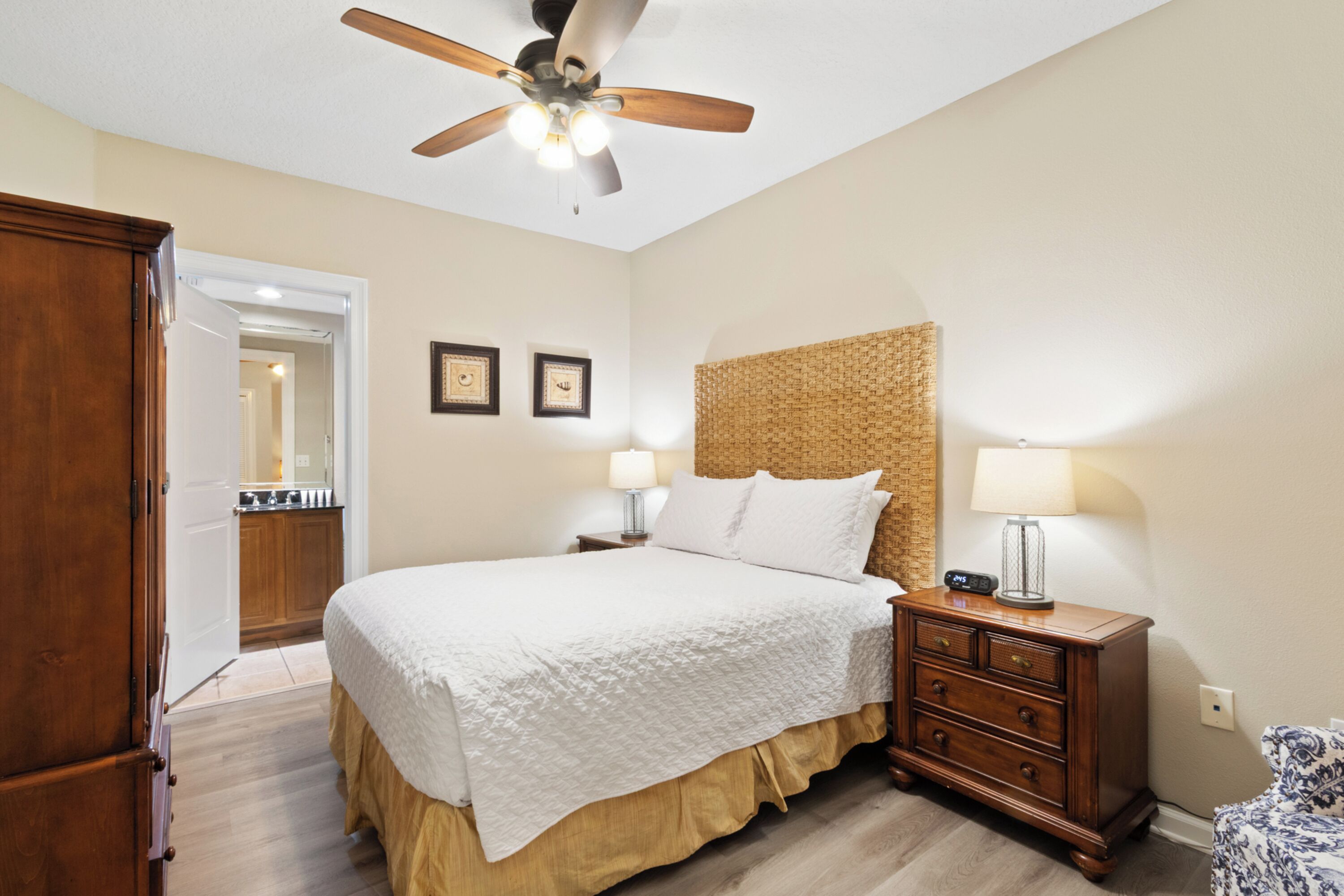 A bedroom with a bed, wooden nightstands, a ceiling fan, and a door leading to another room.