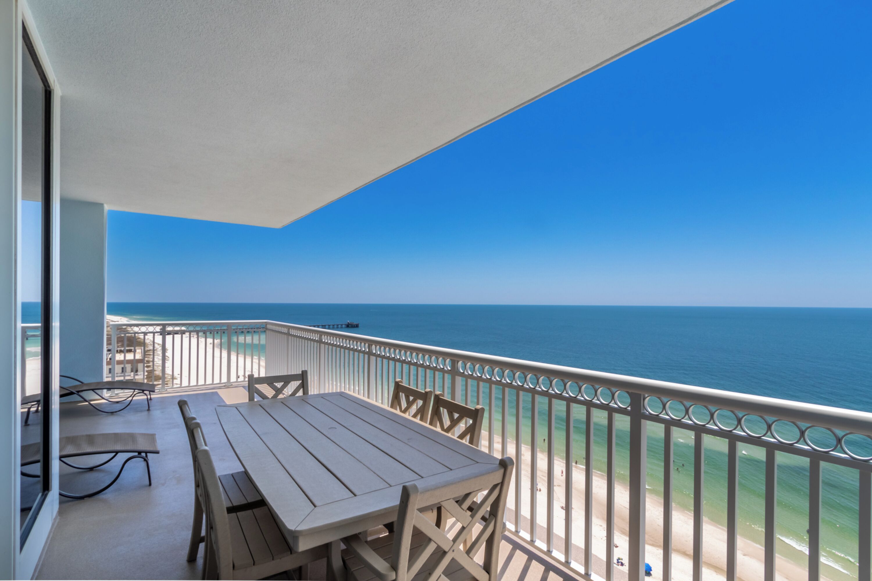 Ein Balkon mit Holztisch und Stühlen, der Blick auf einen Strand und das Meer freigibt.