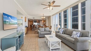 A spacious living room with a grey sofa, a white coffee table, and a TV on the wall. - The Colonnades 1901 (Gulf Shores)