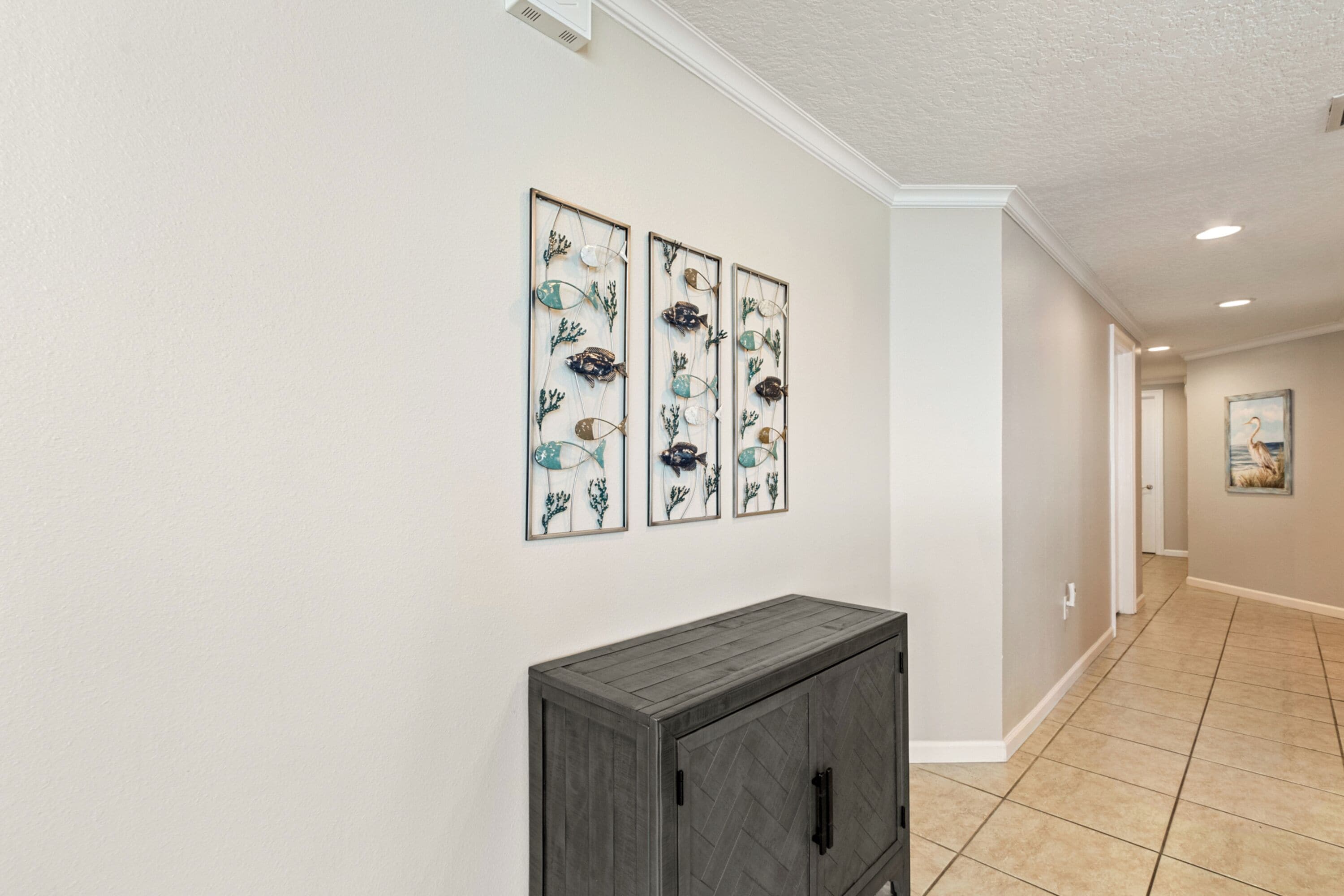 A hallway with a gray cabinet and three framed wall art pieces.