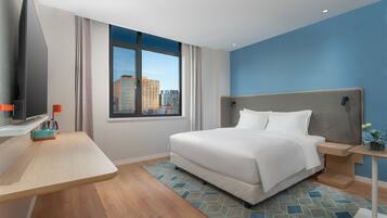 A hotel room with a large bed, a TV, a desk, and a window with a city view.
