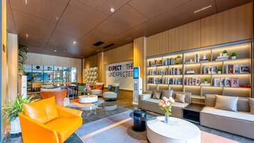 Un moderno vestíbulo de hotel con una zona de estar central, una recepción y una estantería llena de libros y objetos decorativos.