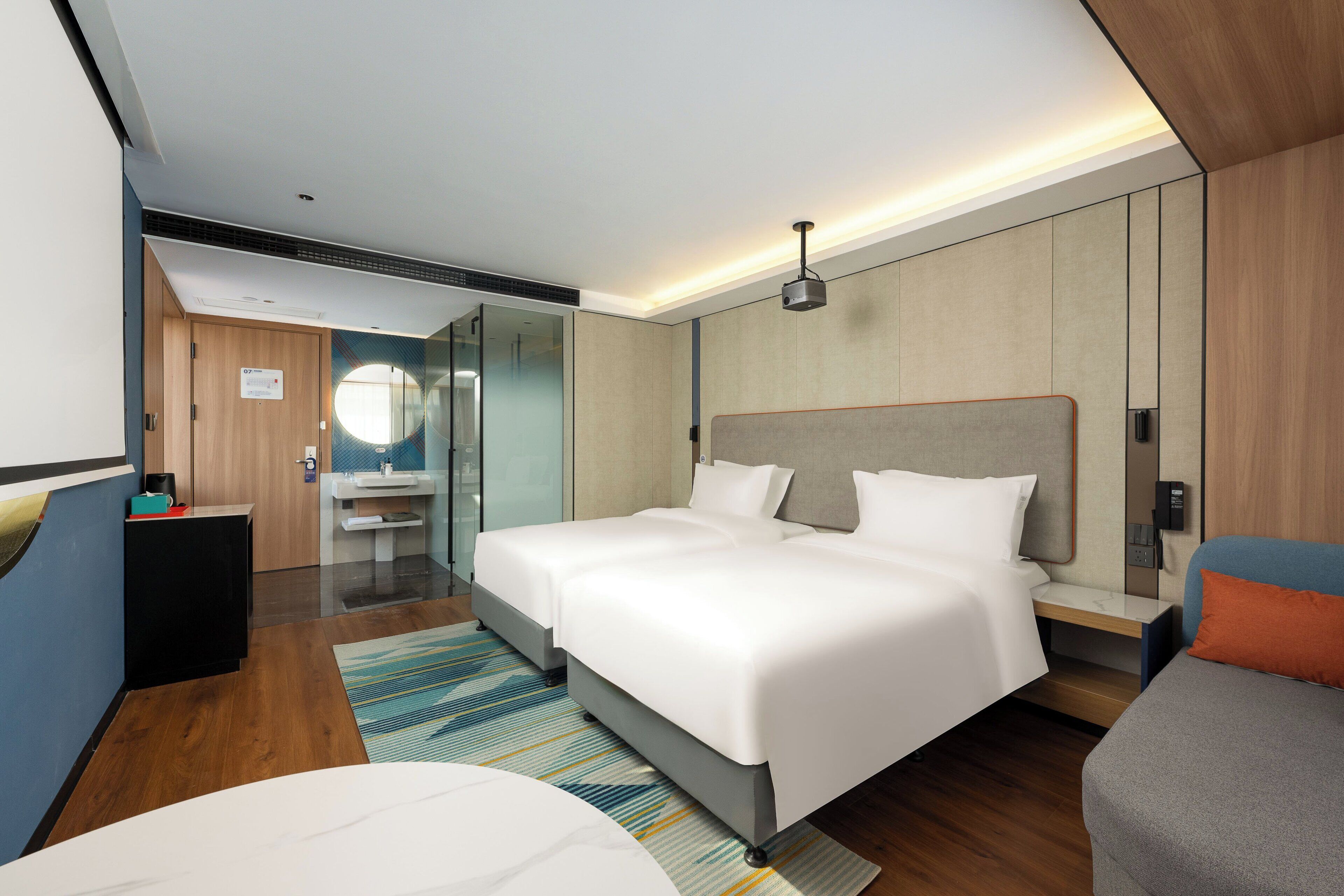 Ein modernes Hotelzimmer mit einem großen Bett, Nachttischen, einem Schreibtisch und einem Badezimmer mit Spiegel und Waschbecken.