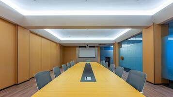 Una sala de conferencias con una larga mesa, sillas, una pantalla de proyector y un muro de cristal azul.