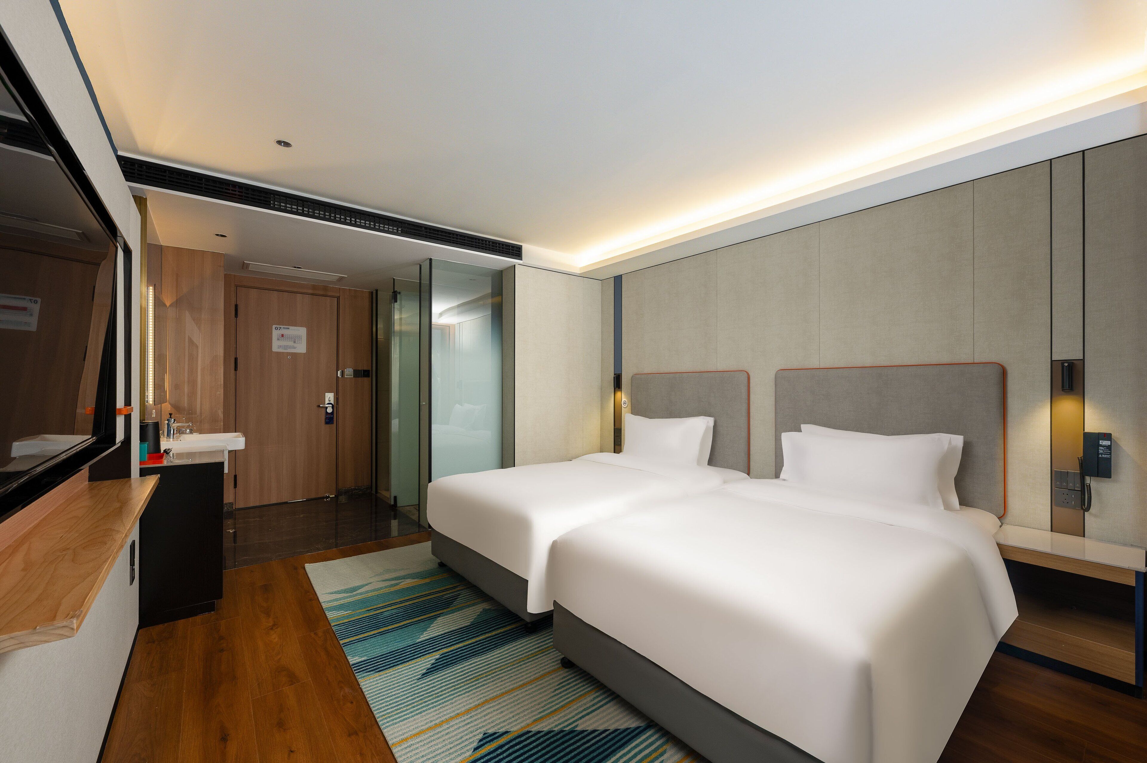 Habitación de hotel con dos camas, un escritorio de madera, un baño y un espejo grande.