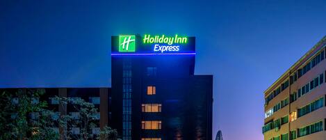 Un edificio de Holiday Inn Express con un letrero visible, rodeado de otros edificios y árboles.