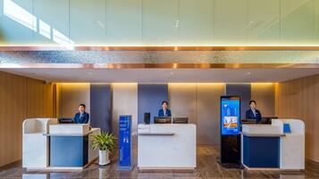 Zona de recepción de un hotel con tres mostradores, cada uno atendido por un recepcionista. A la izquierda, un quiosco de información digital y, a la derecha, una pantalla grande que muestra información del establecimiento.