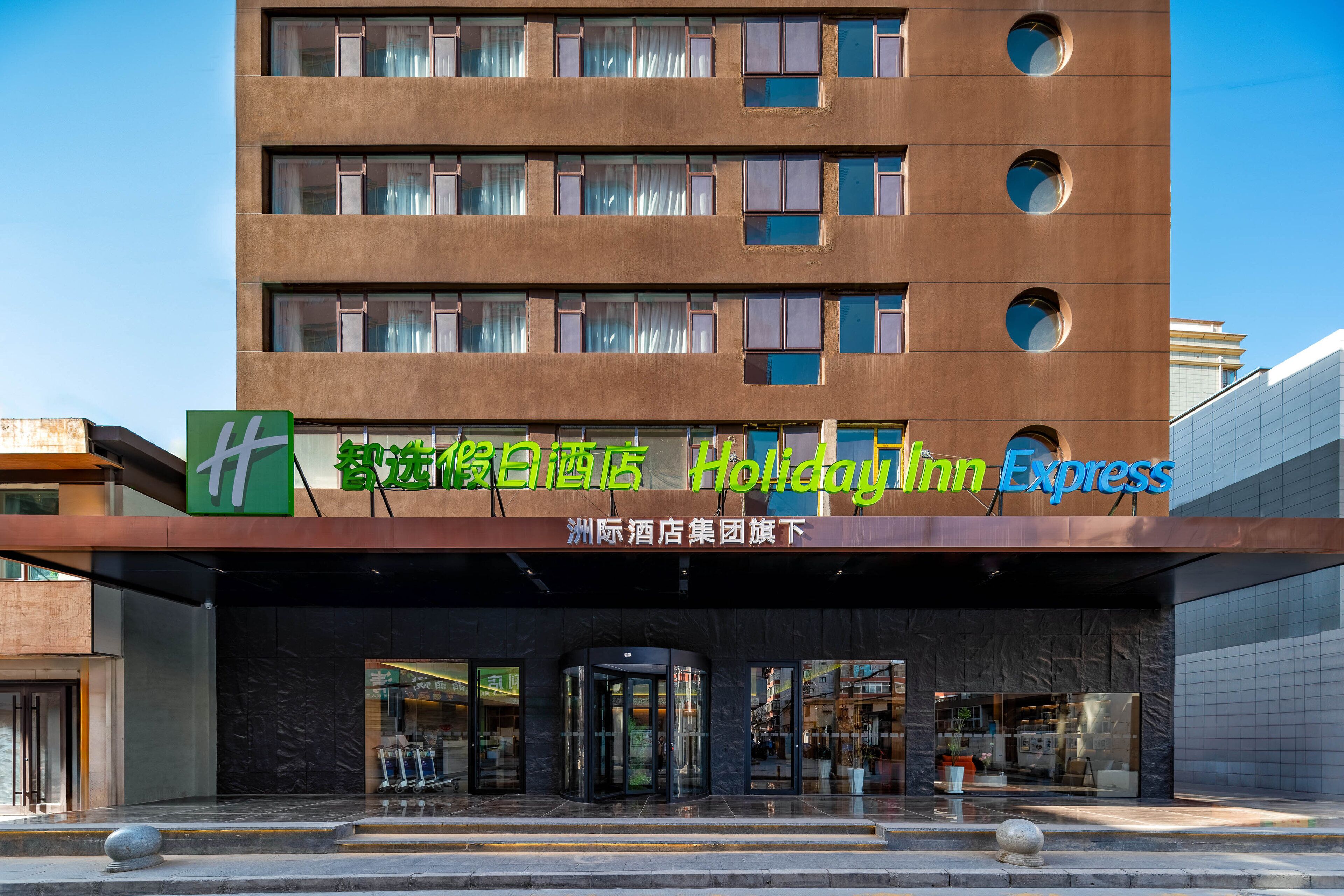 Edificio Holiday Inn Express con fachada moderna, ventanas amplias y una entrada destacada con puerta giratoria.