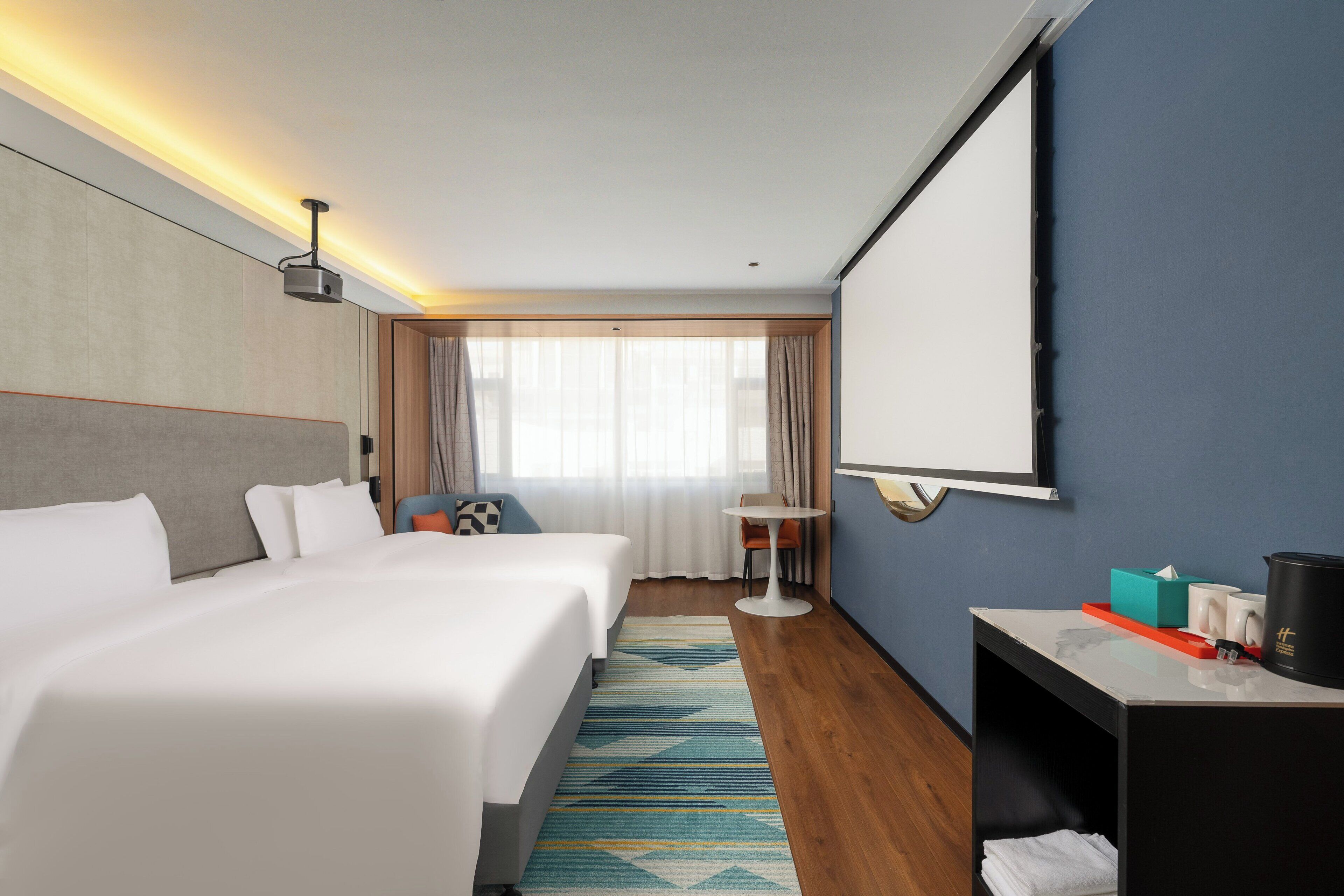 A hotel room with a large bed, a desk with a coffee maker, a small table, and a large mirror.