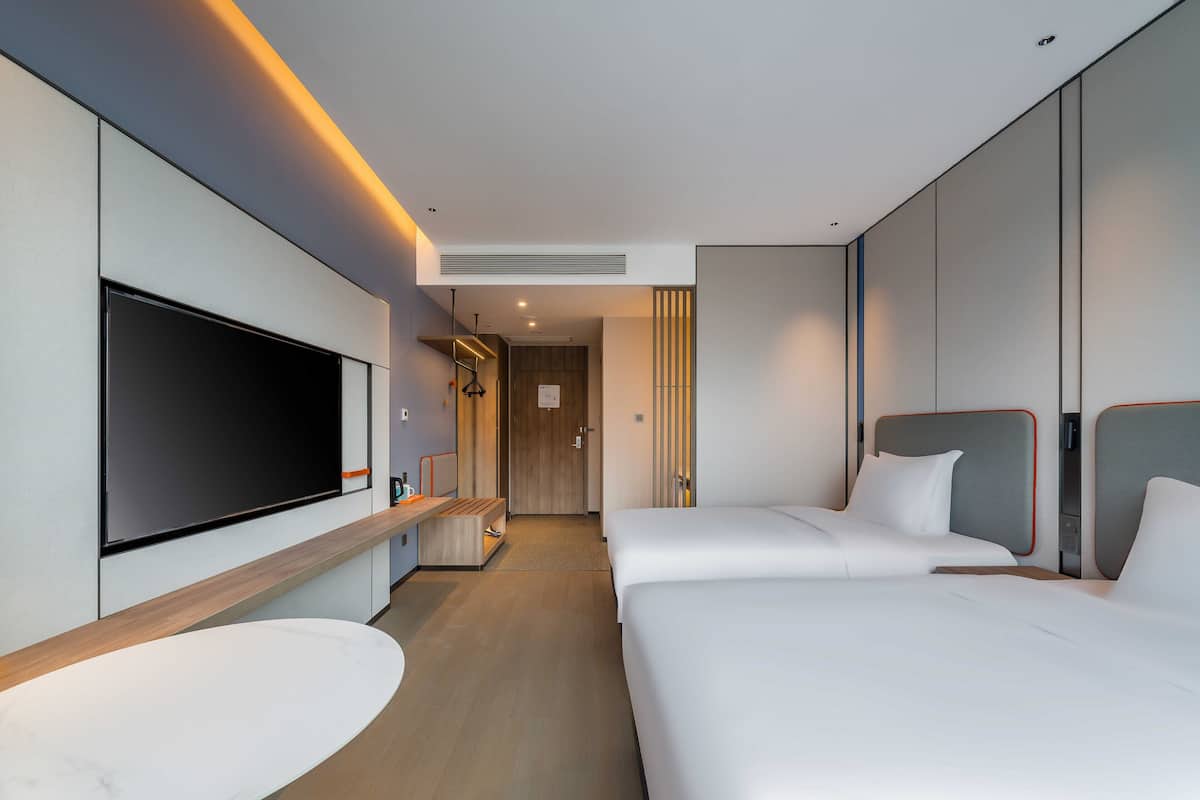 A modern hotel room with a large flat-screen TV, a marble bathroom sink, two beds, and a wooden floor.