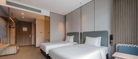 A modern hotel room with two beds, a desk, and a seating area.