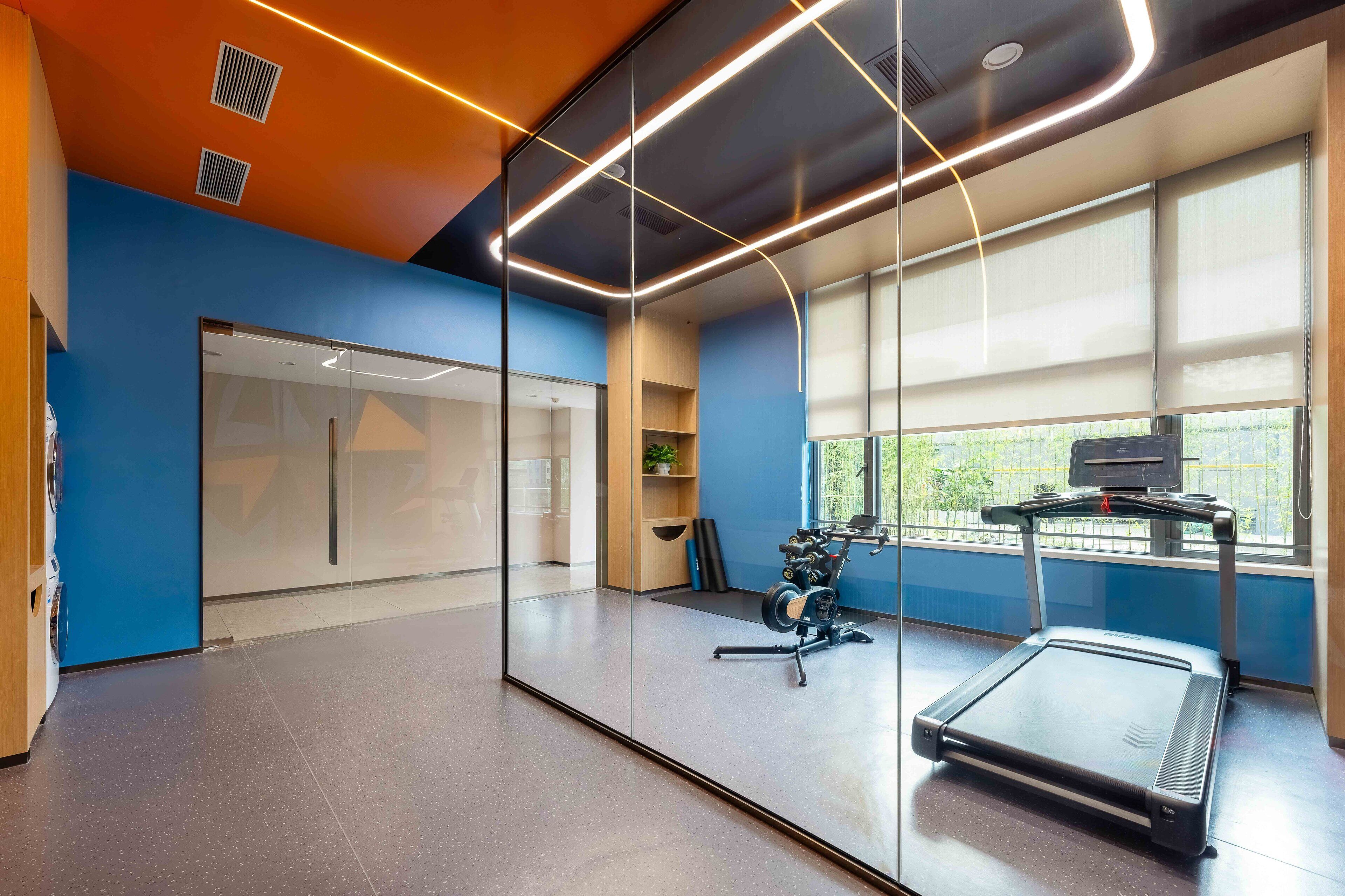 A modern office space with a treadmill, large windows, and a blue wall.