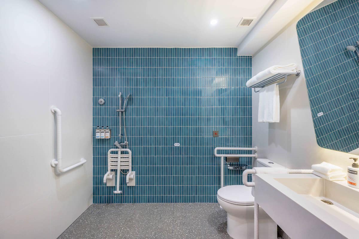A bathroom with a blue tiled wall, a white sink, a toilet, and a shower.
