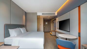 A modern hotel room with a large bed, a TV mounted on the wall, a small round table, and a blue chair.