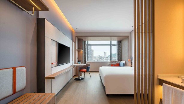 Une chambre d’hôtel moderne dotée d’un grand lit, d’un bureau, d’une chaise, d’une télévision et offrant une vue sur la ville.