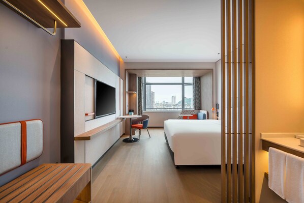 A modern hotel room with a large bed, a desk, a chair, a TV, and a city view. - Holiday Inn Express Jiangmen East Station by IHG (Jiangmen)