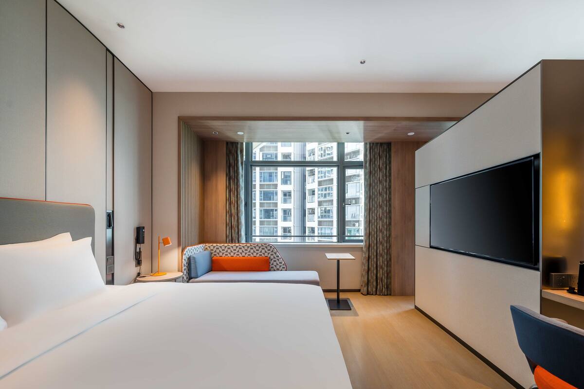 Une chambre d’hôtel moderne avec un grand lit, une télévision et une fenêtre donnant sur la ville.