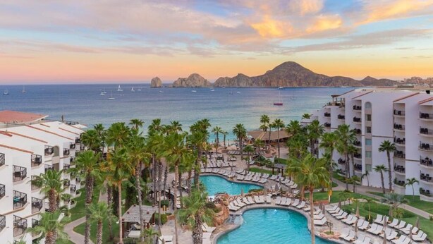 A resort with a pool area, palm trees, and a view of the sea and mountains.