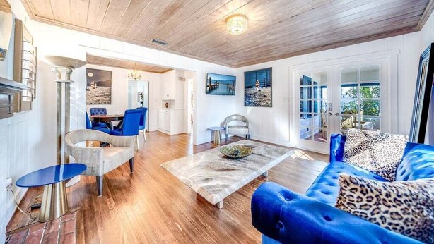 A spacious living room with a wooden ceiling, a blue sofa, a coffee table, and a dining area with blue chairs.