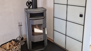 A modern wood-burning stove with a black chimney, a metal ashtray, and a basket of firewood.