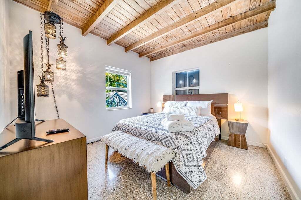 Una camera da letto con soffitto in legno, un letto con lenzuola decorate, un comodino con una lampada e un televisore su un supporto in legno.