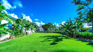 A well-maintained lawn with a clear sky, surrounded by lush greenery and a white building. - 2 BD Delray Beach Cottage walk to Atlantic Ave & the beach (Delray Beach)
