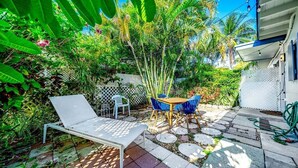 A patio with a white lounge chair, a wooden table, and blue chairs. - 2 BD Delray Beach Cottage walk to Atlantic Ave & the beach (Delray Beach)