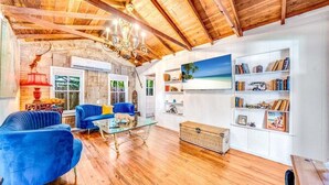 Ein geräumiges Wohnzimmer mit Holzbalkendecke, einem Glastisch, blauen Sofas und einem Bücherregal voller Bücher und Dekoration.