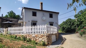 Una casa a due piani con facciata bianca, fondamenta in pietra e un recinto di legno bianco.