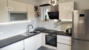 Una cucina moderna con frigorifero in acciaio inossidabile, piano di lavoro nero, mobili bianchi, forno integrato e microonde.