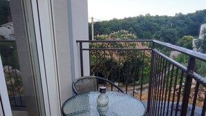 Un balcone con un tavolo in vetro e due sedie in vimini, con vista su un paesaggio verde e rigoglioso.