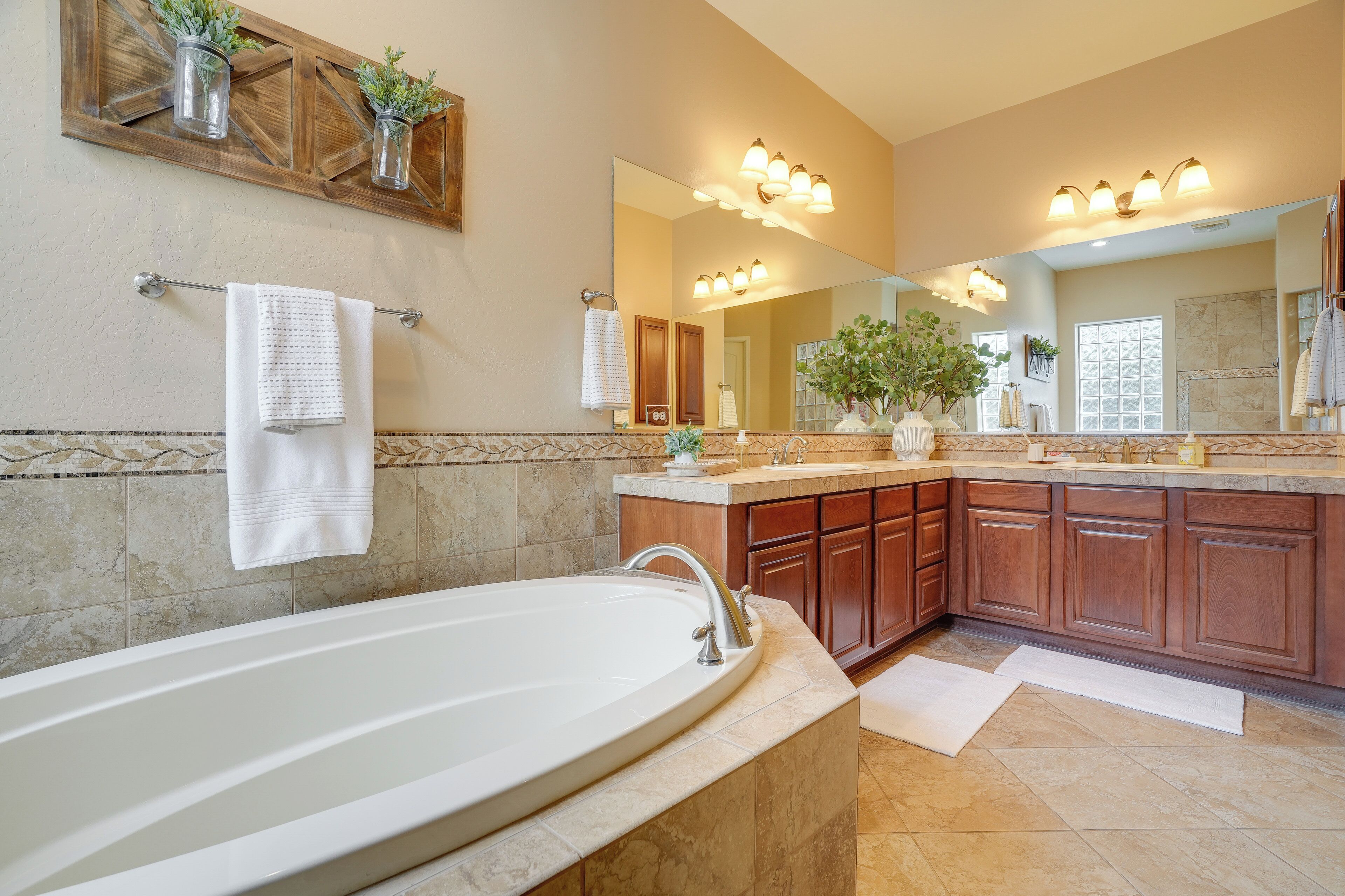 A bathroom with a large bathtub, wooden cabinets, a vanity with a mirror, and a potted plant.