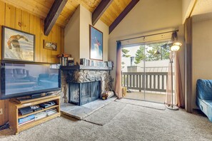 Una sala de estar con chimenea de piedra, estanterías de madera, televisor y un balcón con vistas.