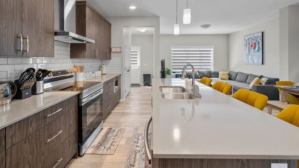 Een moderne keuken met een centraal eiland, houten keukenkastjes en een eethoek met gele stoelen.