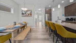 Een moderne keuken met een centraal eiland, een houten eettafel en gele stoelen.
