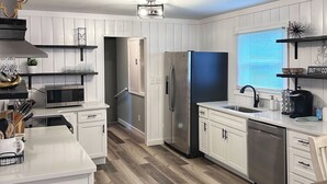 Une cuisine moderne avec des meubles blancs, un réfrigérateur en acier inoxydable et un parquet en bois disposé en motif chevron.