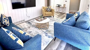 Un salon équipé d’un téléviseur à écran plat, de deux canapés bleus, d’un fauteuil beige et d’une petite table basse ronde.