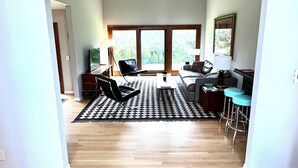 A spacious living area with a large window, a black and white patterned rug, and a wooden floor.
