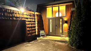 A modern building with a large wooden facade, a glass door entrance, and a seating area with chairs.