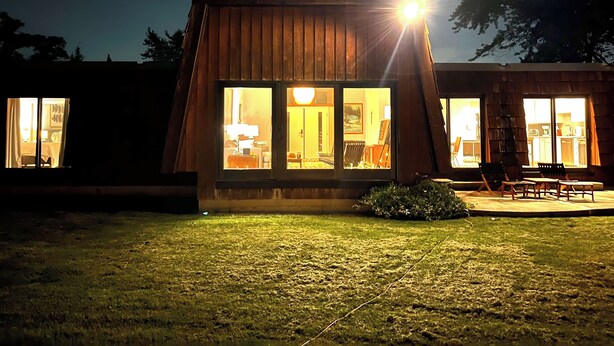 A modern house with large windows, a well-lit interior, and a grassy yard.